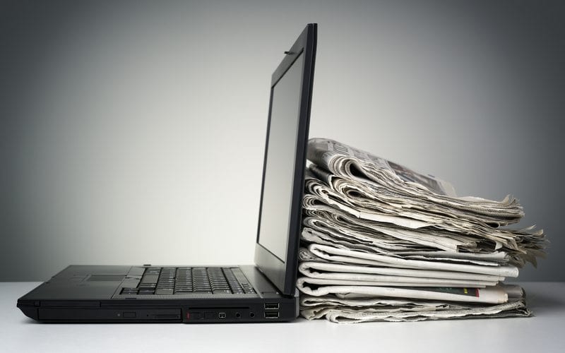 Laptop With Pile Of Newspapers Piled Behind The Screen